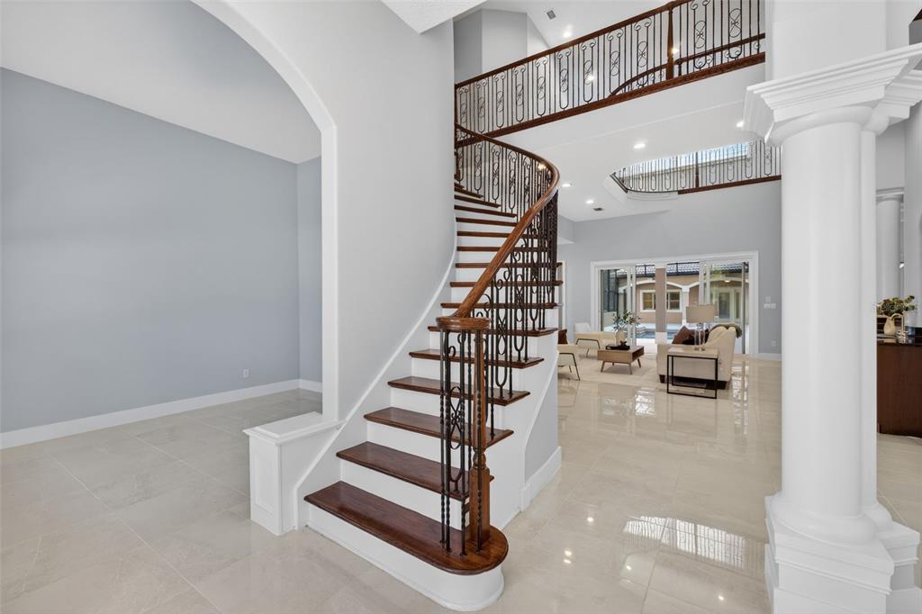 A grand foyer features a curved wooden staircase with iron railings and polished tile floors — 13950 SMOKERISE COURT, ORLANDO, FL