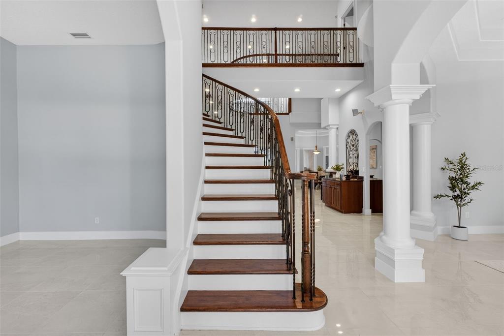 A grand foyer features a curved wooden staircase with iron railings and white tile flooring — 13950 SMOKERISE COURT, ORLANDO, FL