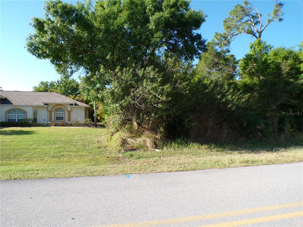 A grassy lot with dense trees and shrubs sits next to a single-story house — 25161 AYSEN DRIVE, PUNTA GORDA, FL