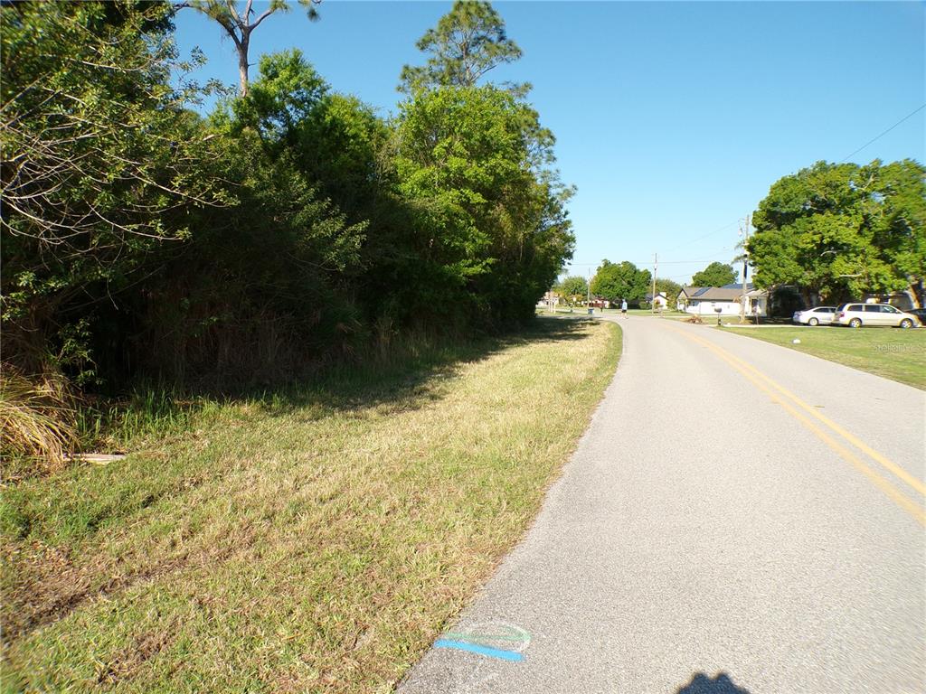 A paved road runs alongside a grassy shoulder and a dense line of trees — 25161 AYSEN DRIVE, PUNTA GORDA, FL