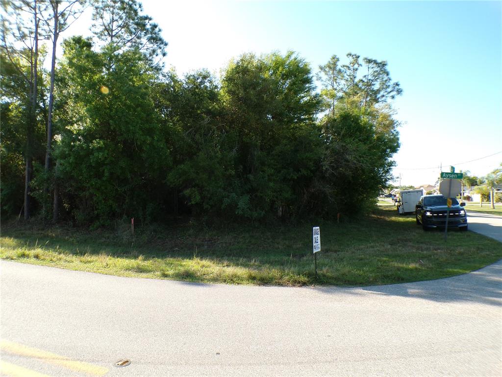A vacant, wooded corner lot sits at a road intersection with a parked truck nearby — 25161 AYSEN DRIVE, PUNTA GORDA, FL