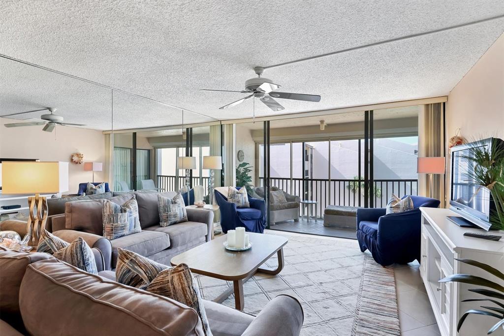 A living room features a gray sofa, blue armchairs, a coffee table, and a mirrored wall — 6480 MIDNIGHT PASS ROAD UNIT 506, SARASOTA, FL