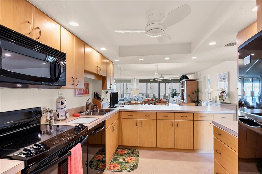 A kitchen with light wood cabinets, black appliances, and a breakfast bar overlooking the living area — 6480 MIDNIGHT PASS ROAD UNIT 506, SARASOTA, FL