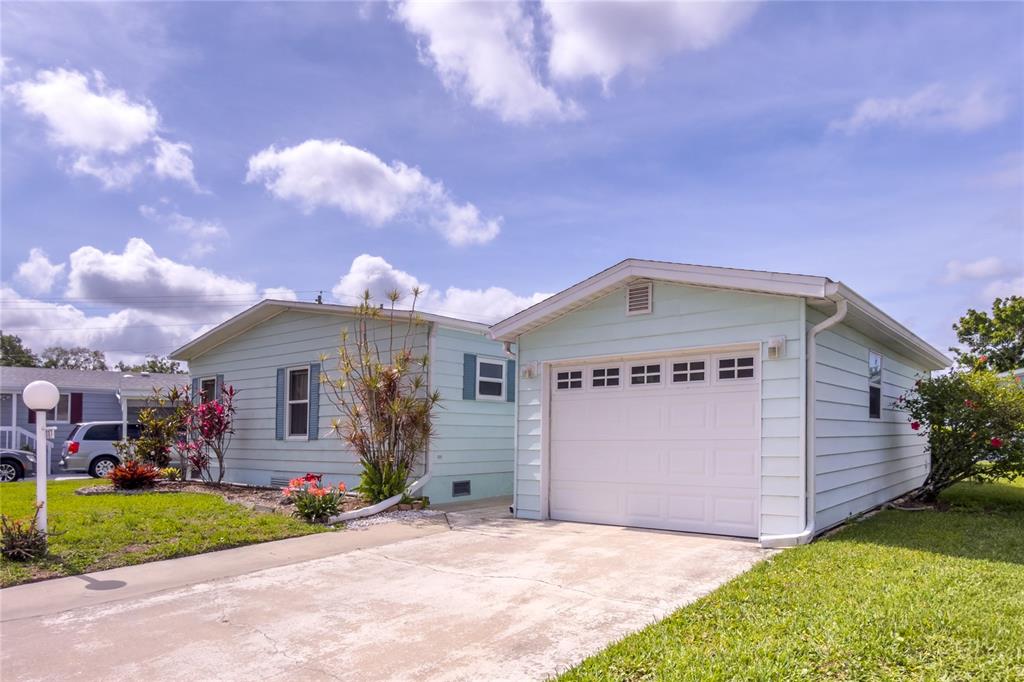A light blue house with a white garage and a concrete driveway under a cloudy sky — 117 HERON COURT, ELLENTON, FL
