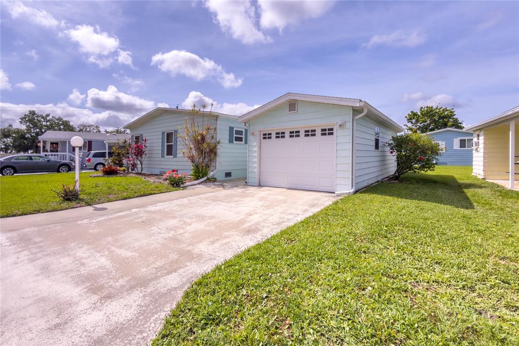 A light blue house with a white garage and a concrete driveway under a cloudy sky — 117 HERON COURT, ELLENTON, FL