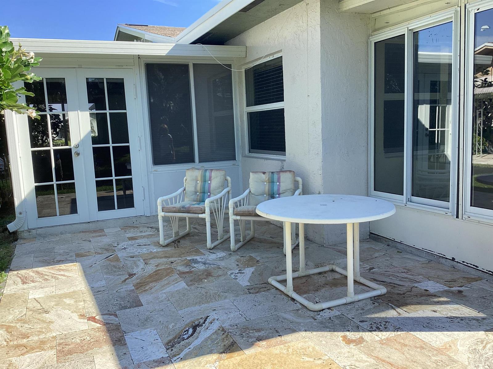 A patio with two chairs and a round table sits outside a white house — 13861 Packard Terrace, Delray Beach FL 33484, DELRAY BEACH, FL