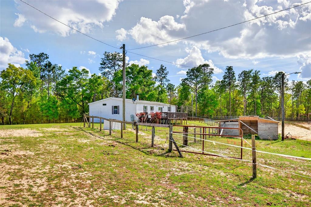 A white house with a wooden deck sits behind a fenced pasture and shed — 16170 SW 30TH LANE, OCALA, FL