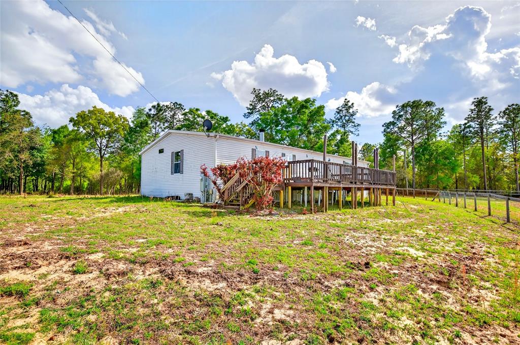 A white single-story house features a large wooden deck and is surrounded by trees — 16170 SW 30TH LANE, OCALA, FL