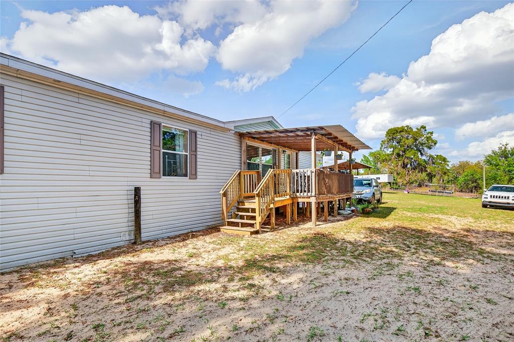 A light-colored mobile home features a wooden deck with a covered patio area — 16170 SW 30TH LANE, OCALA, FL