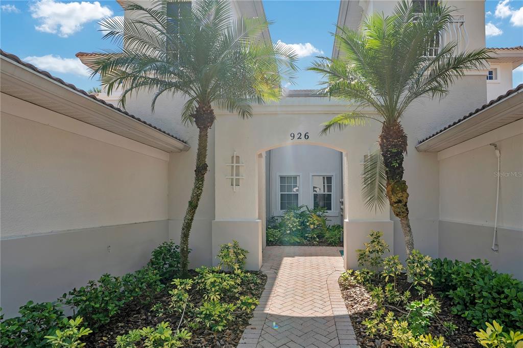 A brick walkway leads to the arched entryway of a two-story home with palm trees — 926 RIVER BASIN COURT UNIT 201C, BRADENTON, FL