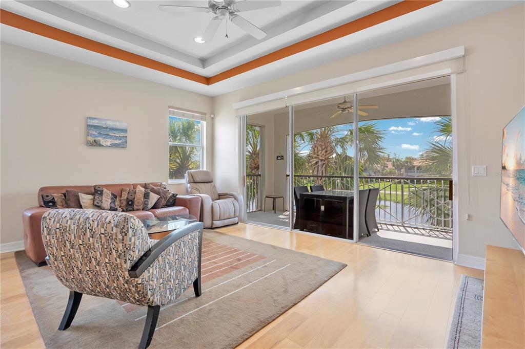 A living room with light wood floors, a tray ceiling, and sliding doors to a balcony — 926 RIVER BASIN COURT UNIT 201C, BRADENTON, FL