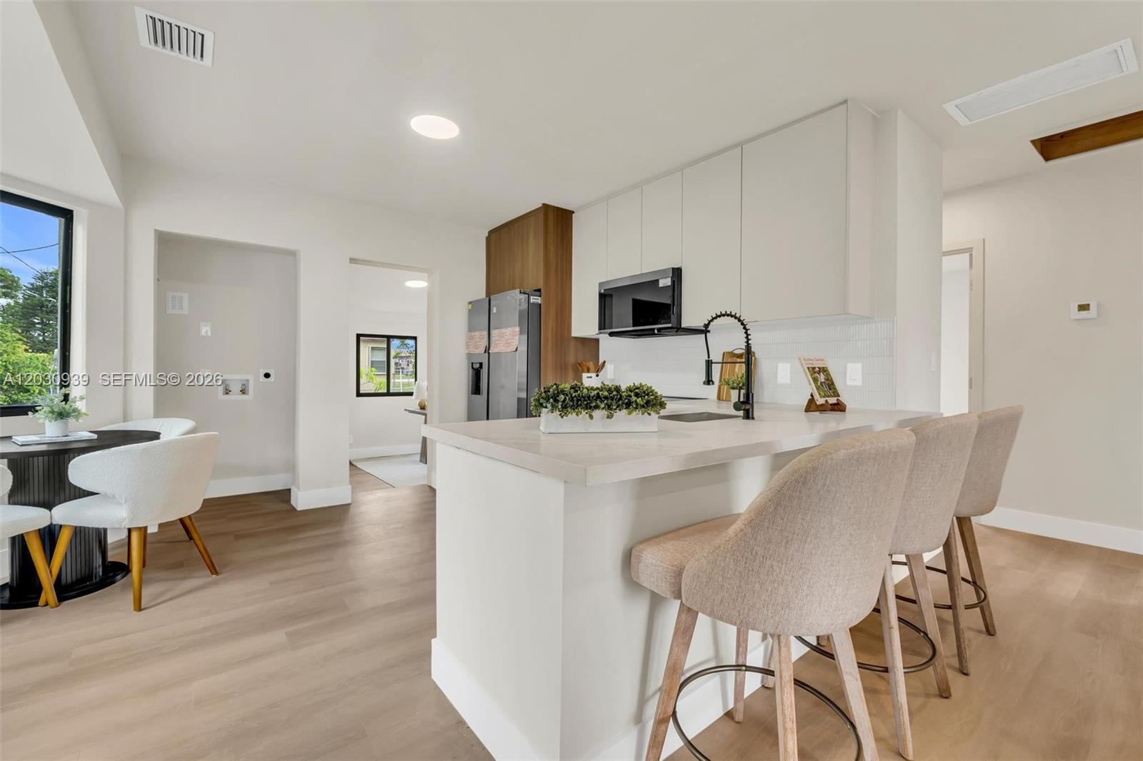 A modern kitchen features white cabinetry, a stone-topped island, and light wood-look flooring — 2651 Fletcher Ct, Hollywood FL 33020, HOLLYWOOD, FL