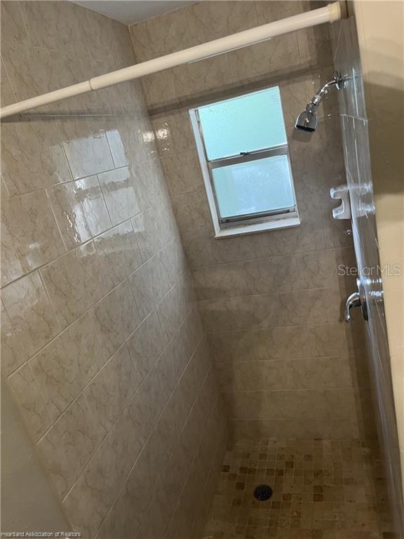 A tiled walk-in shower features a small window, a showerhead, and a floor drain — 231 S ORANGE STREET, SEBRING, FL