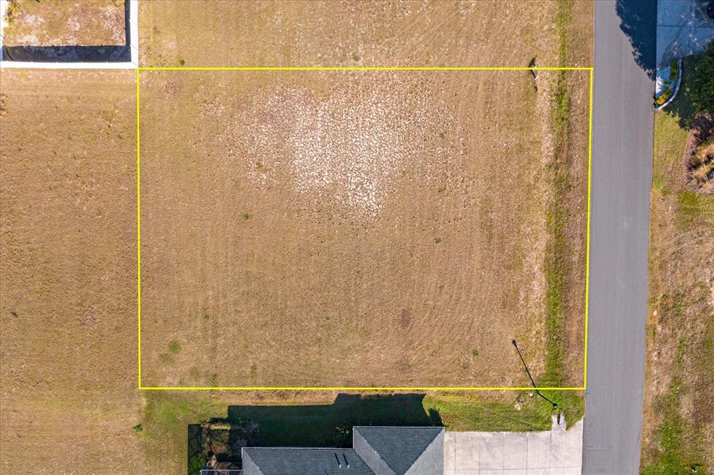 An aerial view shows a rectangular vacant residential lot outlined in yellow next to a road — 1114 MYRTLE BREEZES COURT, FRUITLAND PARK, FL