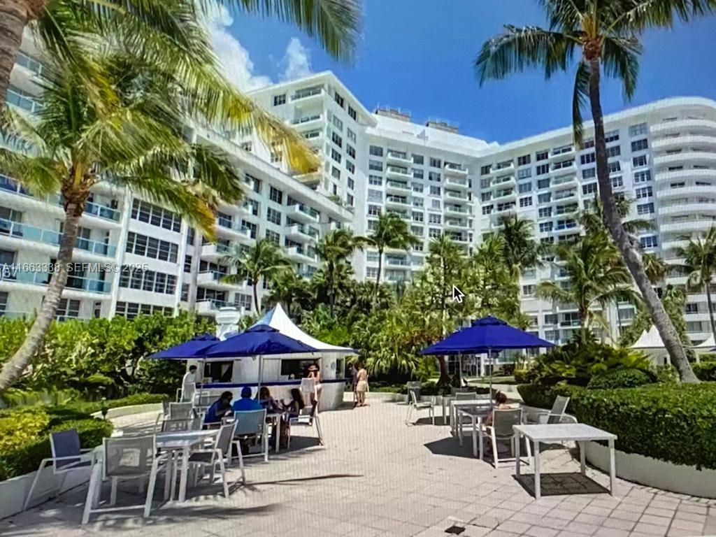 An outdoor patio area with tables, chairs, and blue umbrellas in front of a large building — 5151 Collins Ave # 925, Miami Beach FL 33140, MIAMI BEACH, FL