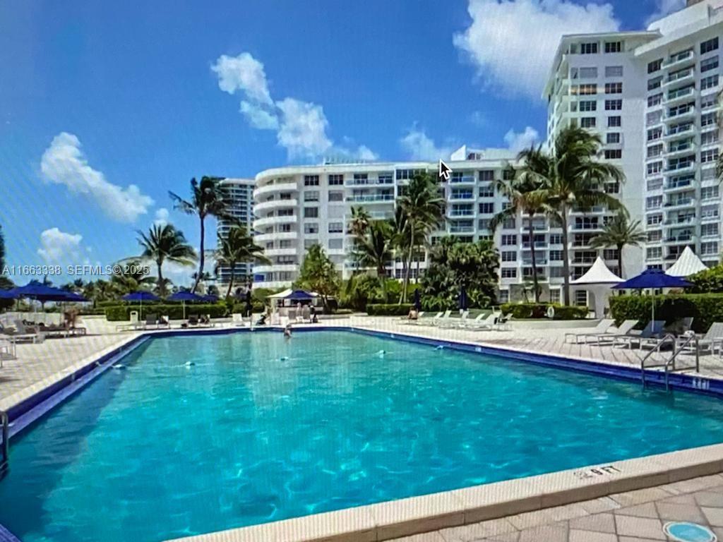 A large outdoor swimming pool sits in front of a multi-story white apartment building — 5151 Collins Ave # 925, Miami Beach FL 33140, MIAMI BEACH, FL