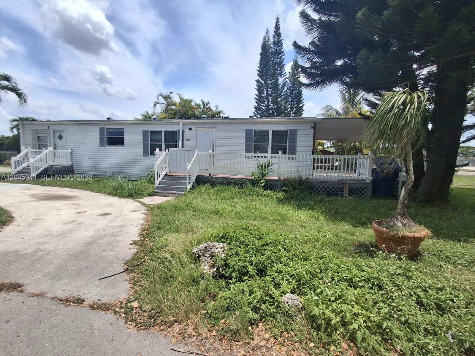 A single-story mobile home features white siding, a wooden deck, and a concrete driveway — 19800 SW 180 Ave, Miami FL 33187, MIAMI, FL