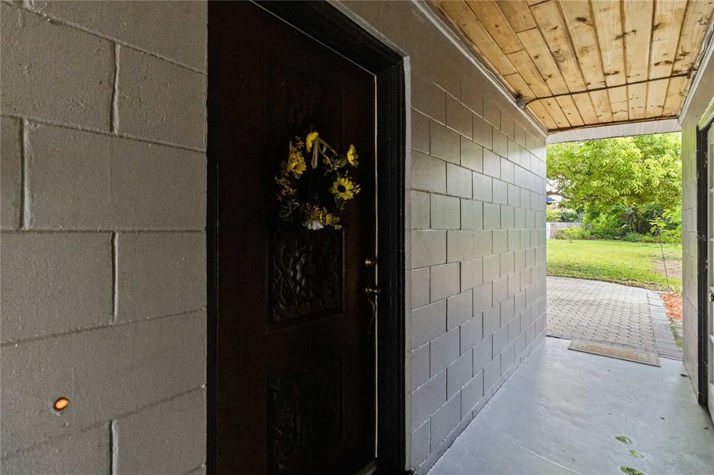 A dark wooden front door with a floral wreath sits on a covered concrete porch — 407 S SUNLAND DRIVE, SANFORD, FL