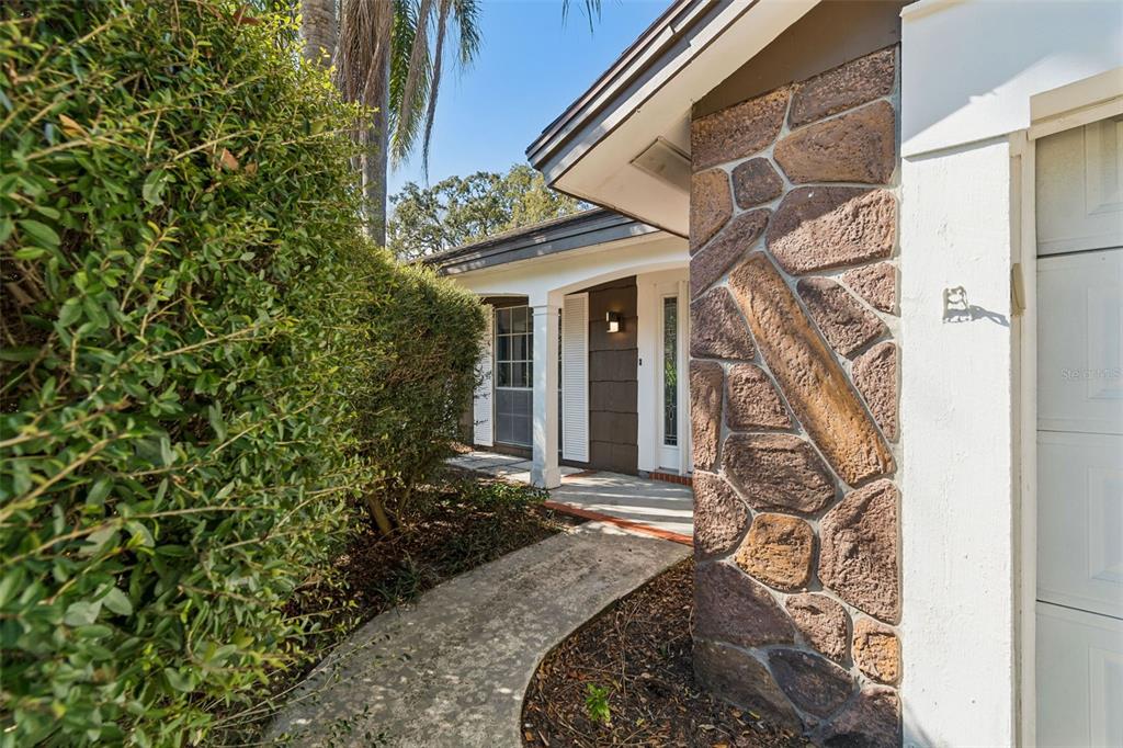 A stone-accented exterior wall stands beside a concrete walkway leading to a home entrance — 8210 CLOVER HILL LOOP, HUDSON, FL