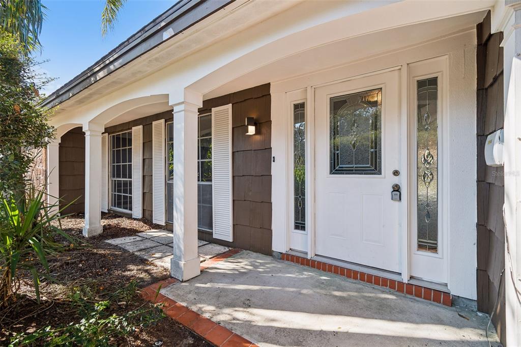 A front porch with a white door, sidelights, and brown shingle siding under a covered entryway — 8210 CLOVER HILL LOOP, HUDSON, FL