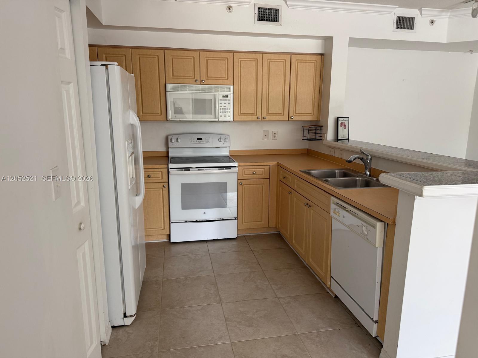 A kitchen features light wood cabinets, white appliances, tan countertops, and tiled flooring — 6861 SW 44th St # 205, Miami FL 33155, MIAMI, FL