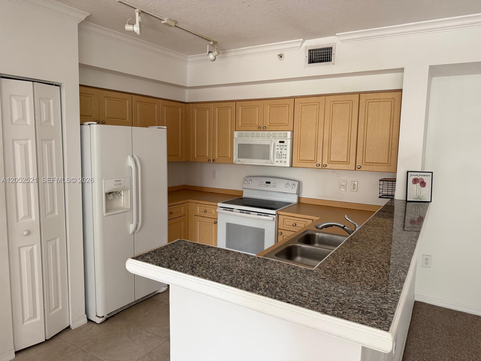 A kitchen features light wood cabinets, white appliances, and a granite-topped peninsula counter — 6861 SW 44th St # 205, Miami FL 33155, MIAMI, FL