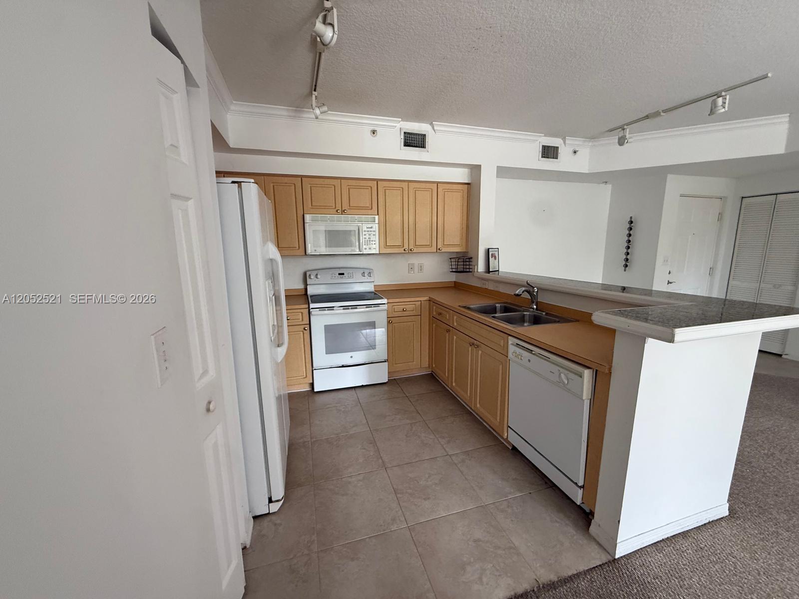 A kitchen features light wood cabinets, white appliances, tile flooring, and a granite-topped breakfast bar — 6861 SW 44th St # 205, Miami FL 33155, MIAMI, FL