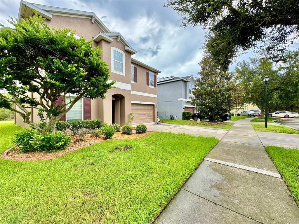 A two-story tan house with a garage, front lawn, and sidewalk under a cloudy sky — 9614 OAK GLADE AVENUE, TAMPA, FL