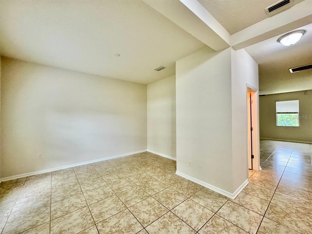 An empty room with beige tile flooring and white walls leads to an adjacent hallway — 9614 OAK GLADE AVENUE, TAMPA, FL