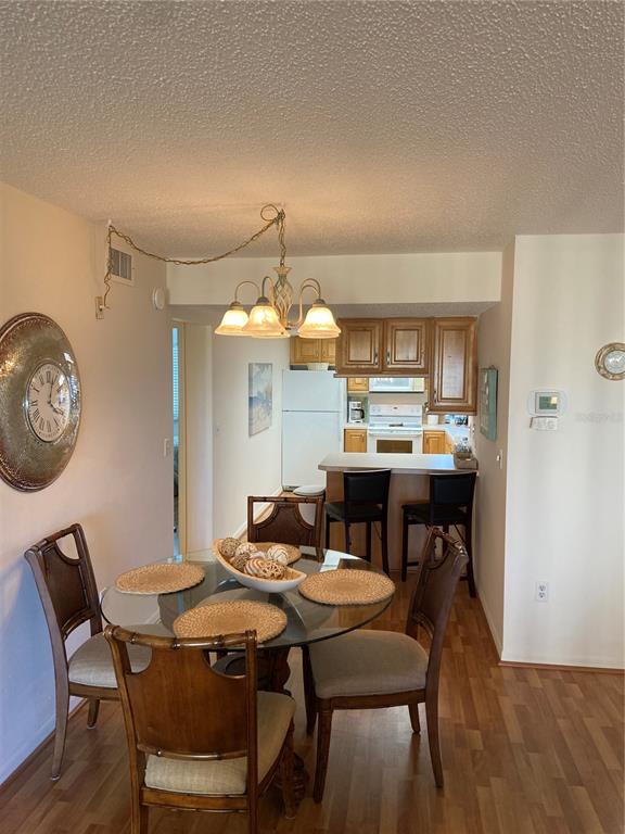 A dining area with a glass table and chairs leads into a kitchen with wood cabinets — 700 GOLDEN BEACH BOULEVARD UNIT 131, VENICE, FL