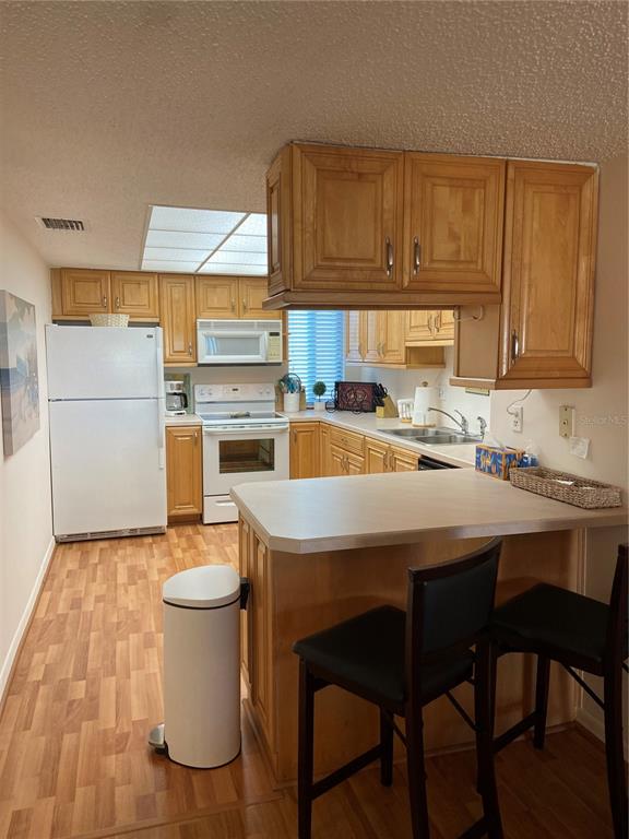 A kitchen features light wood cabinets, white appliances, a breakfast bar, and wood-look flooring — 700 GOLDEN BEACH BOULEVARD UNIT 131, VENICE, FL