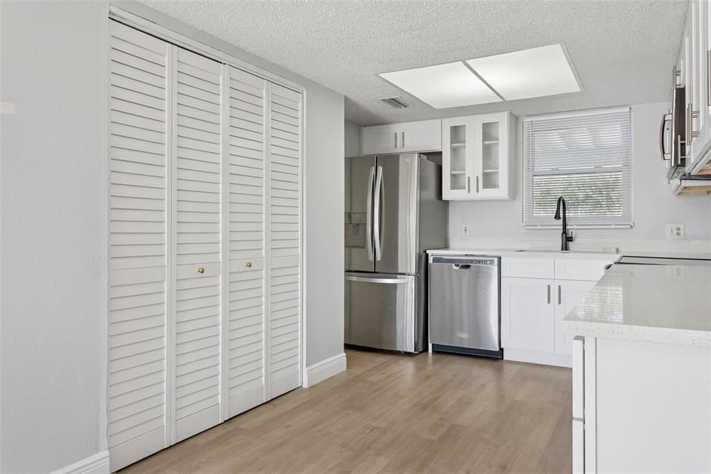 A kitchen features white cabinets, stainless steel appliances, a window, and light wood-look flooring — 5110 TENNIS COURT CIRCLE UNIT 86, TAMPA, FL