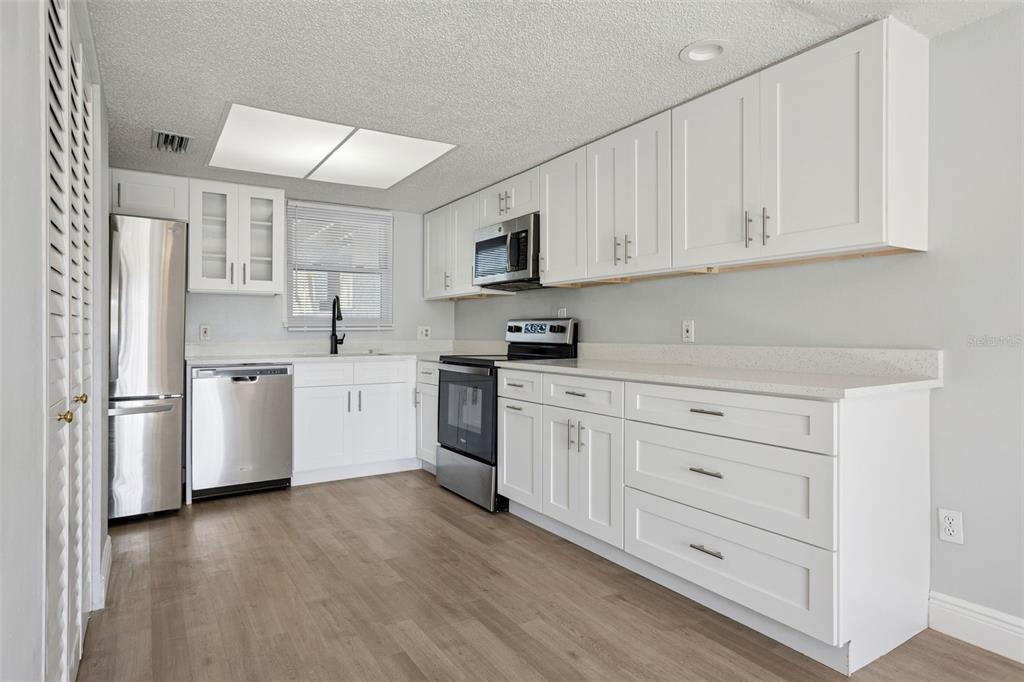 A kitchen with white cabinets, stainless steel appliances, and light wood-look flooring — 5110 TENNIS COURT CIRCLE UNIT 86, TAMPA, FL