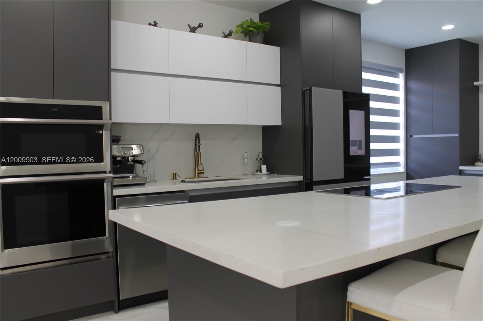A modern kitchen features dark gray cabinetry, white upper cabinets, and a large white island — 1114 Tupelo Way, Weston FL 33327, WESTON, FL