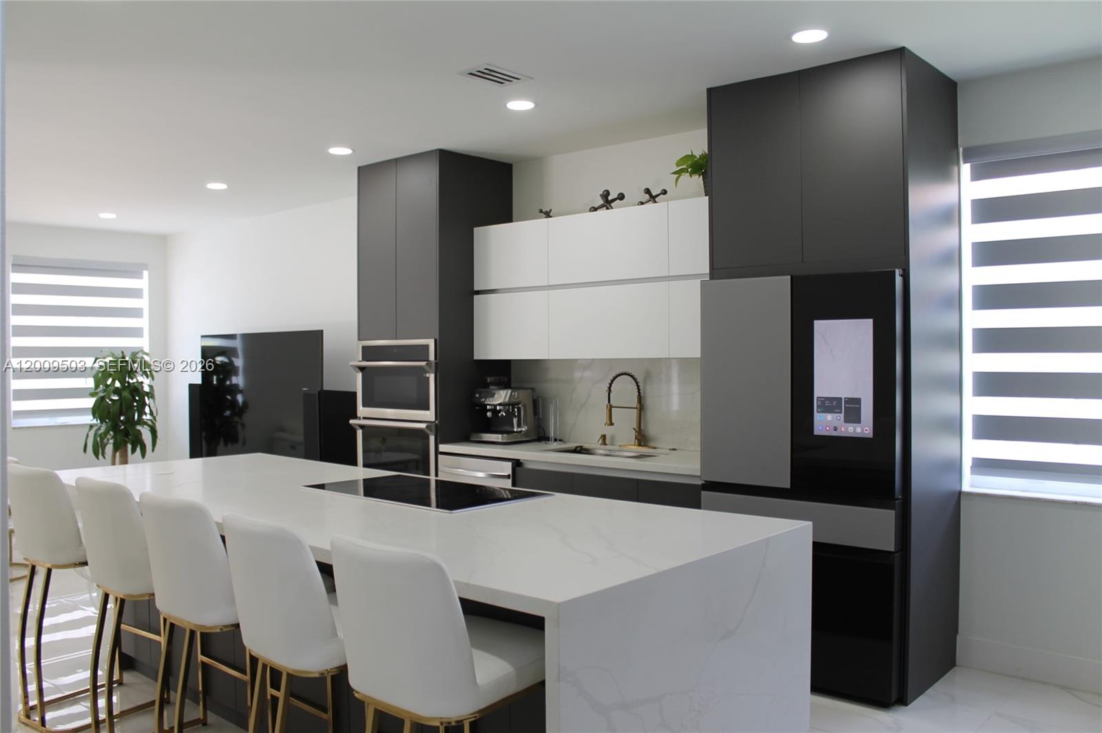 A modern kitchen features a white waterfall island, dark cabinetry, and a smart refrigerator — 1114 Tupelo Way, Weston FL 33327, WESTON, FL