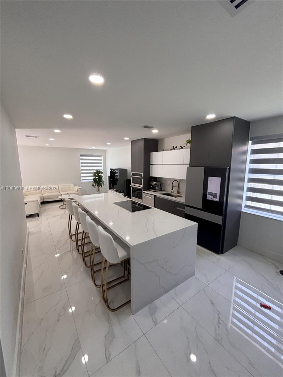 A modern kitchen features a large marble-topped island, dark cabinetry, and white tile flooring — 1114 Tupelo Way, Weston FL 33327, WESTON, FL