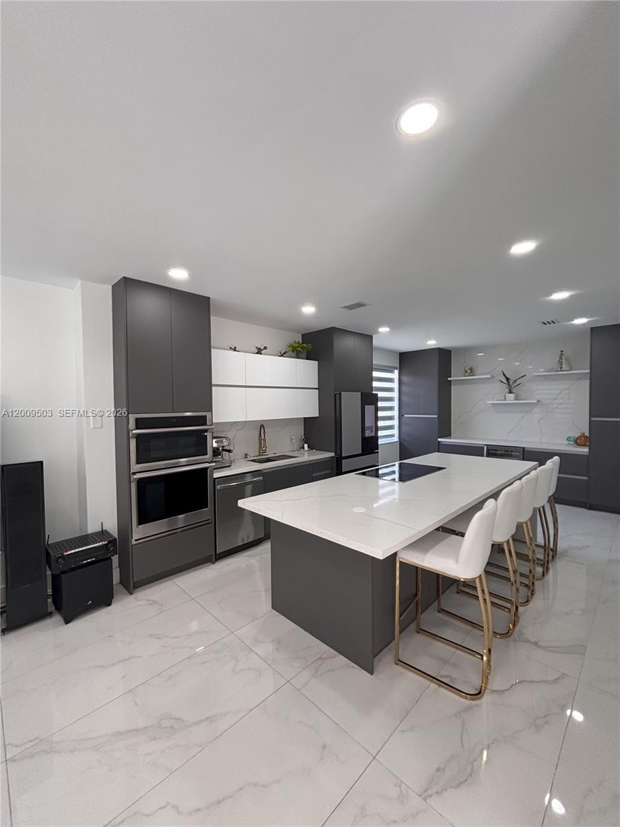 A modern kitchen features dark grey cabinetry, white upper cabinets, and a large marble-topped island — 1114 Tupelo Way, Weston FL 33327, WESTON, FL