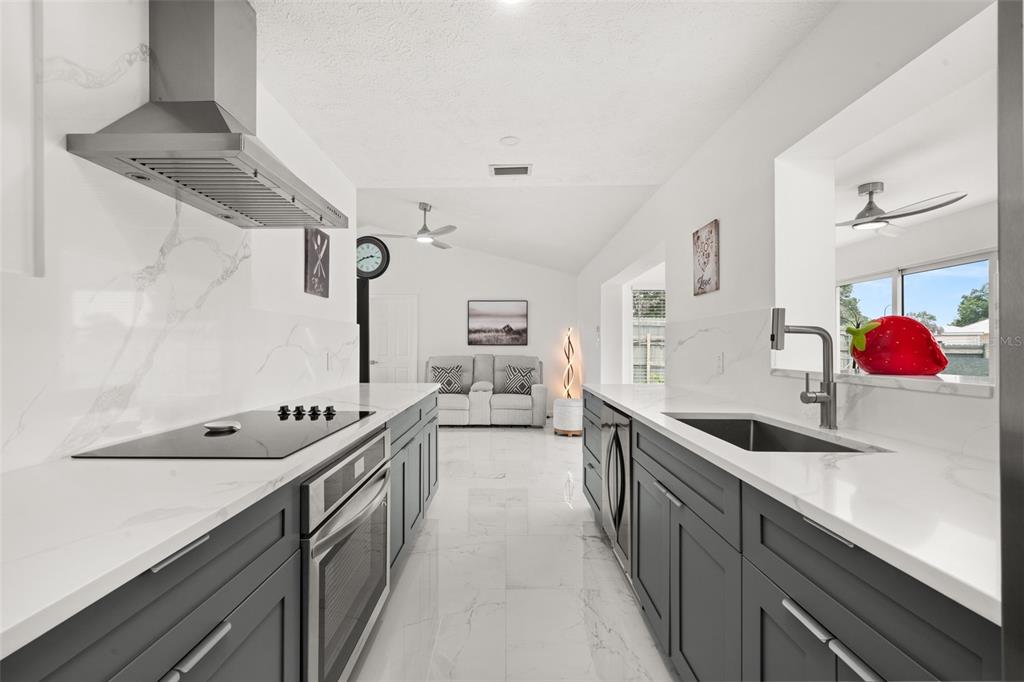 A modern galley kitchen features dark gray cabinetry, white marble countertops, and stainless steel appliances — 4224 LAKE VISTA DRIVE, SEBRING, FL