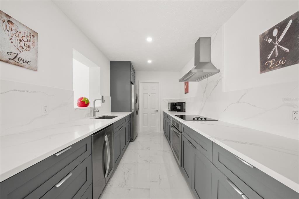 A galley kitchen features gray cabinets, white marble-look countertops, and stainless steel appliances — 4224 LAKE VISTA DRIVE, SEBRING, FL