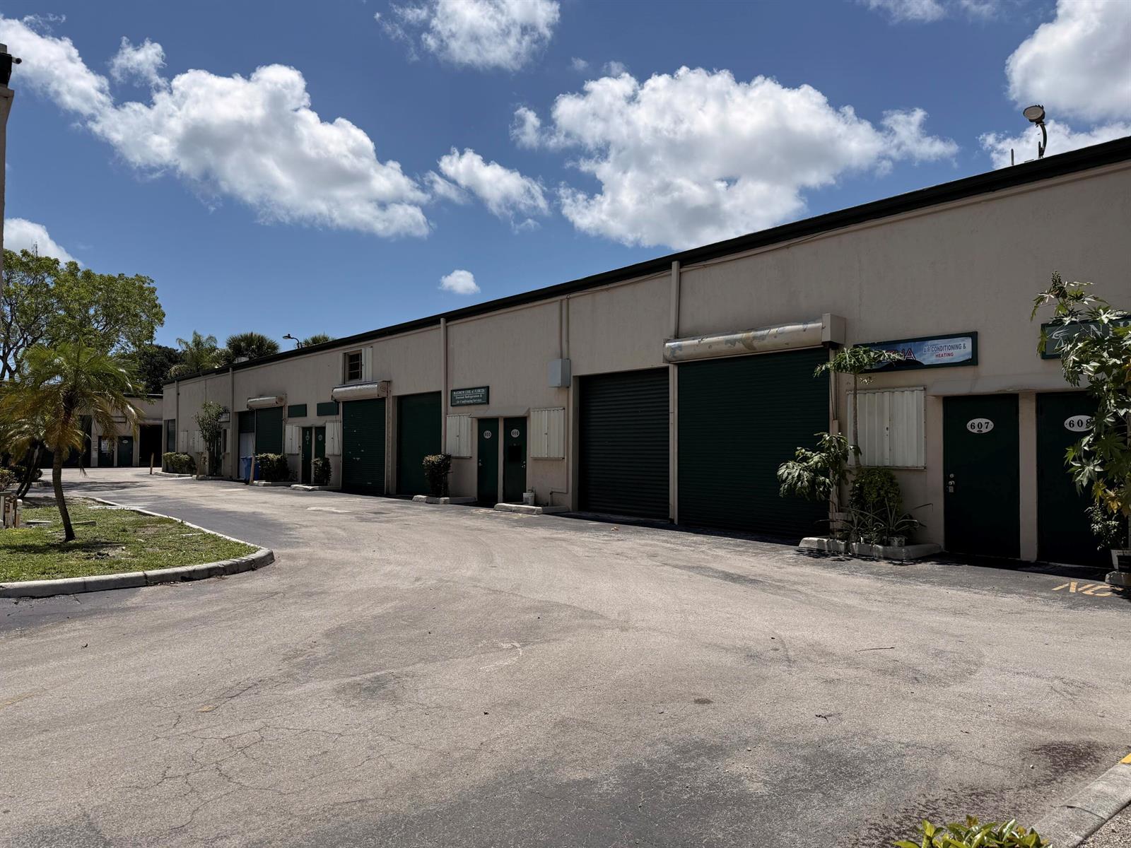 An exterior view of a single-story commercial warehouse building with multiple roll-up doors and entrances — 1791 Blount Road # 606, Pompano Beach FL 33069, POMPANO BEACH, FL