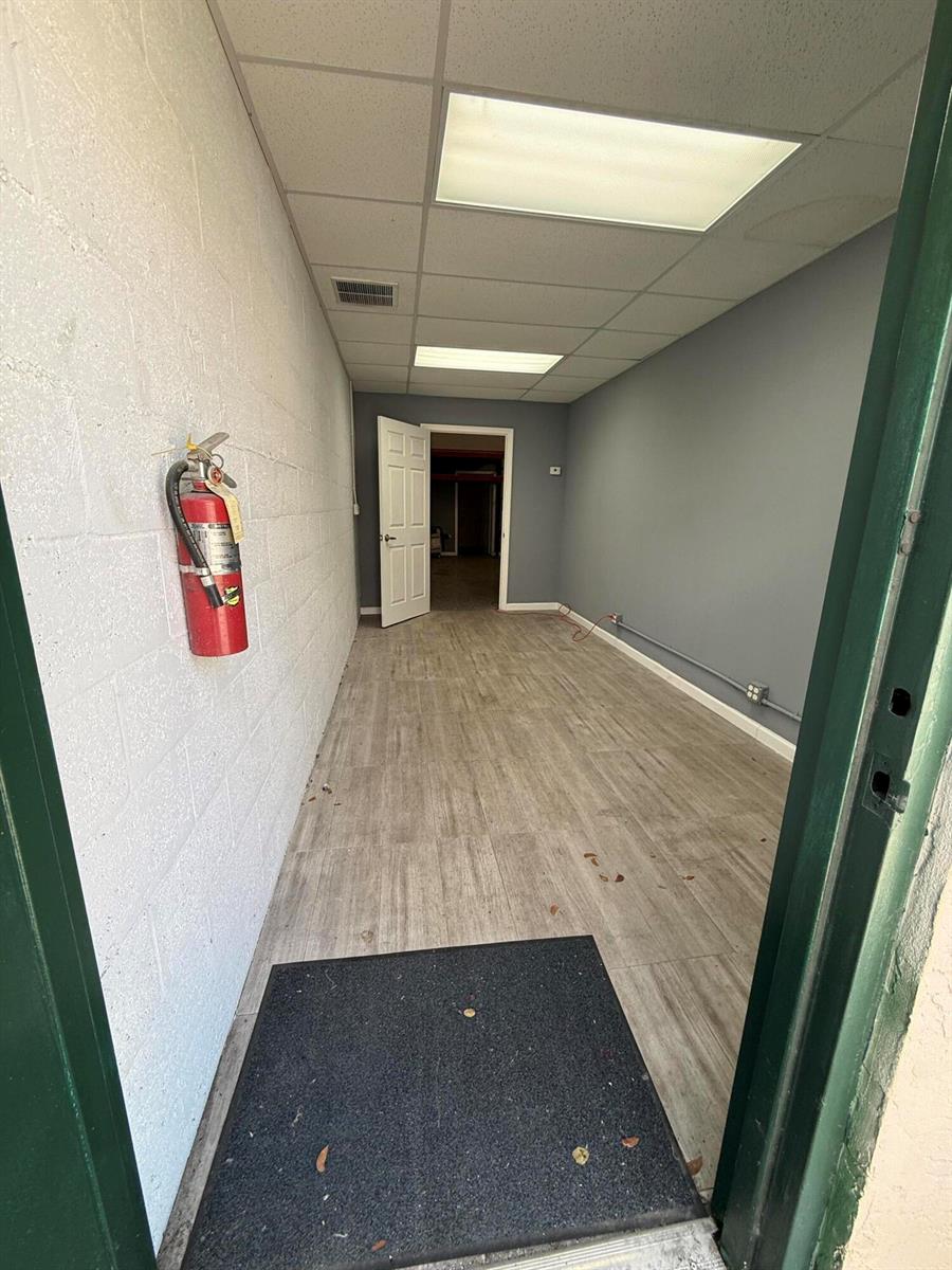 A narrow, empty office space features light wood-look flooring, gray walls, and a fire extinguisher — 1791 Blount Road # 606, Pompano Beach FL 33069, POMPANO BEACH, FL