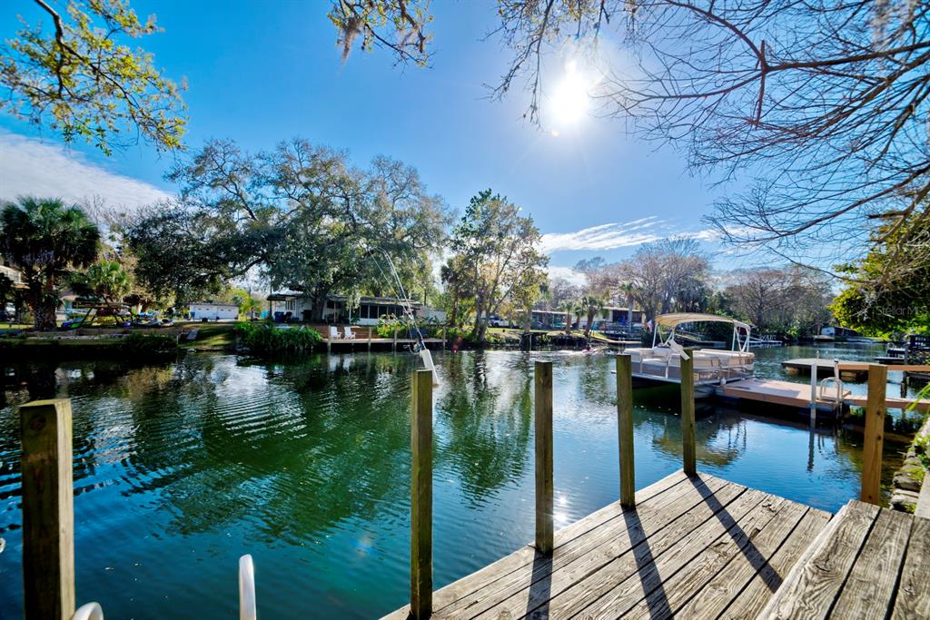 A wooden dock overlooks a calm canal with a pontoon boat moored nearby — 6427 W RICHARD DRIVE, WEEKI WACHEE, FL