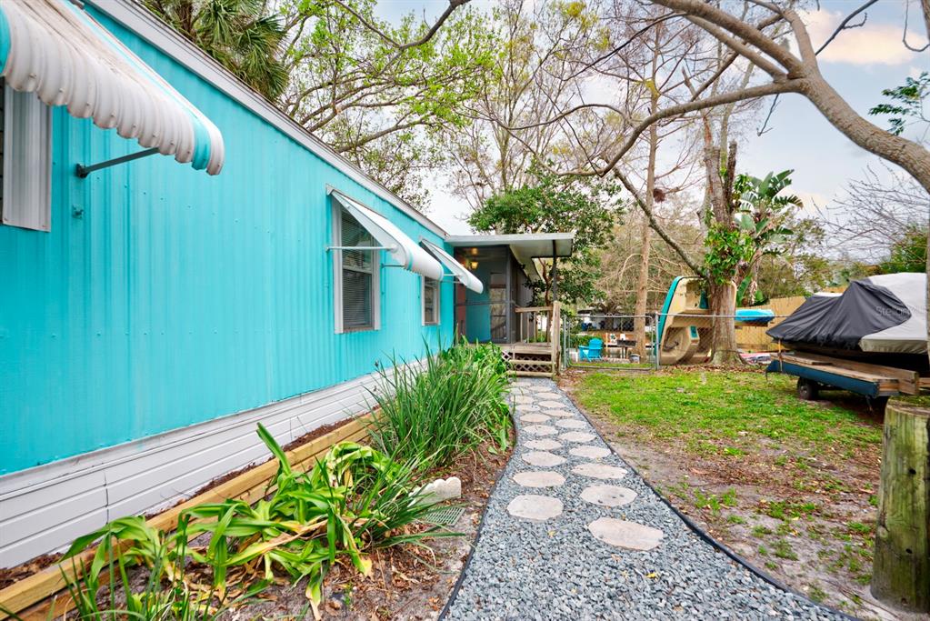 A teal mobile home features a stone walkway leading to a screened porch and yard — 6427 W RICHARD DRIVE, WEEKI WACHEE, FL