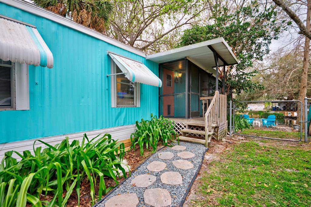 A teal mobile home features a screened-in porch, a stone walkway, and metal window awnings — 6427 W RICHARD DRIVE, WEEKI WACHEE, FL