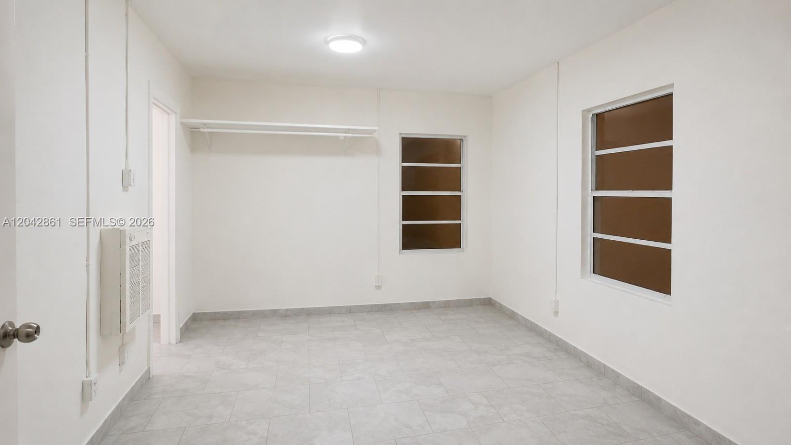 An empty room with white walls, gray tile flooring, two windows, and a wall shelf — 240 SW 6th St # 1, Belle Glade FL 33430, BELLE GLADE, FL