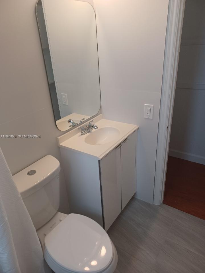 A small bathroom features a white vanity, a rounded mirror, and a toilet — 6950 Byron Ave # 7, Miami Beach FL 33141, MIAMI BEACH, FL
