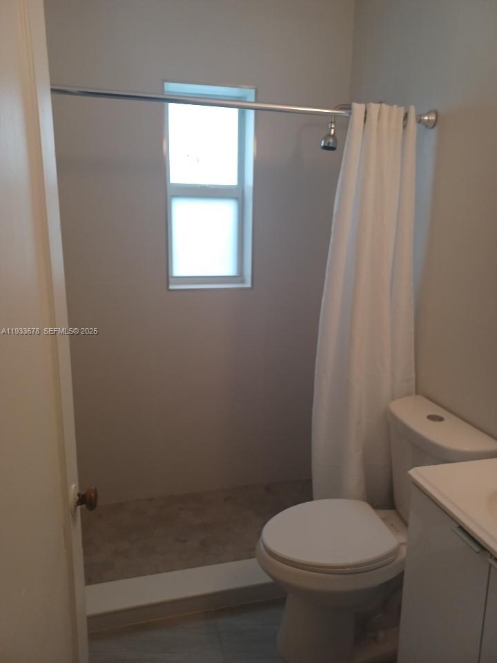 A bathroom features a walk-in shower with a window, a toilet, and a vanity — 6950 Byron Ave # 7, Miami Beach FL 33141, MIAMI BEACH, FL
