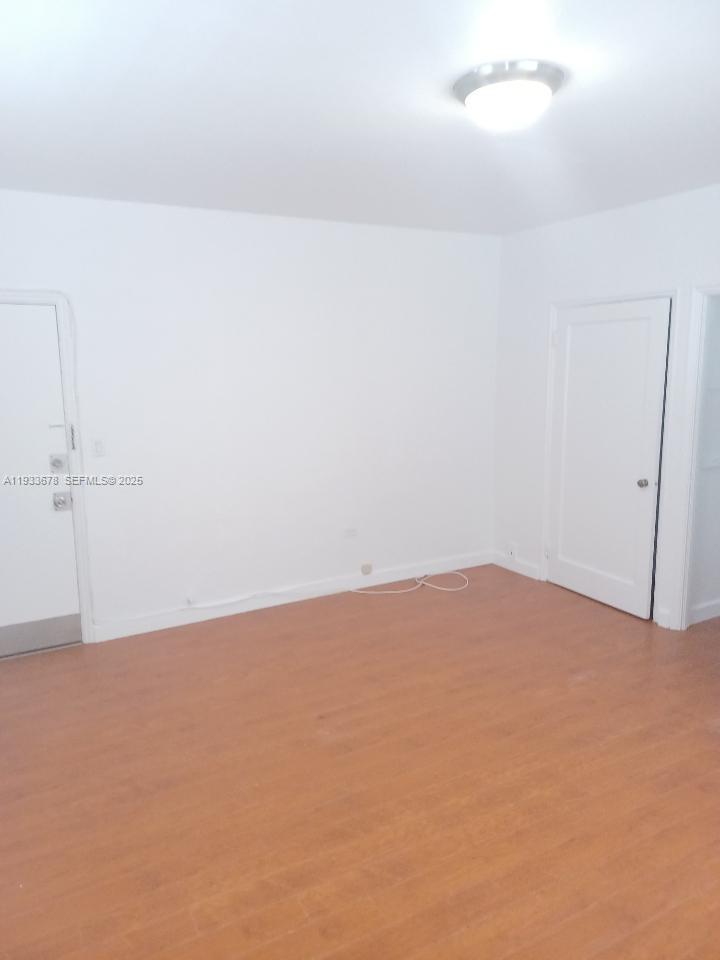 An empty room features white walls, light wood-look flooring, and two white doors — 6950 Byron Ave # 7, Miami Beach FL 33141, MIAMI BEACH, FL