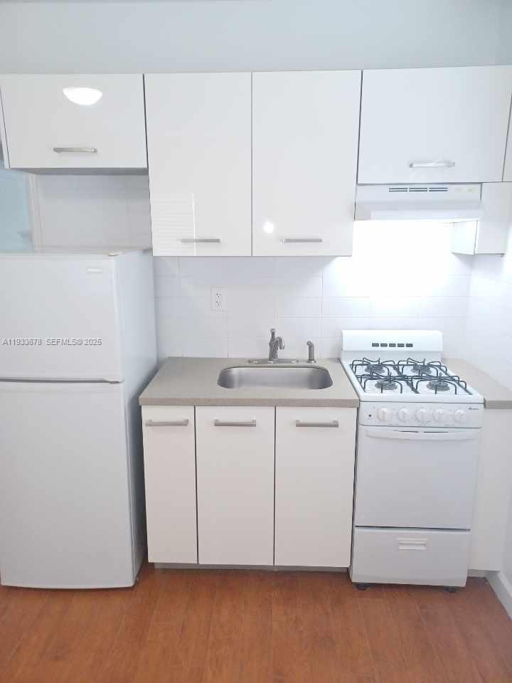 A small kitchen features white cabinets, a refrigerator, a sink, and a gas stove — 6950 Byron Ave # 7, Miami Beach FL 33141, MIAMI BEACH, FL