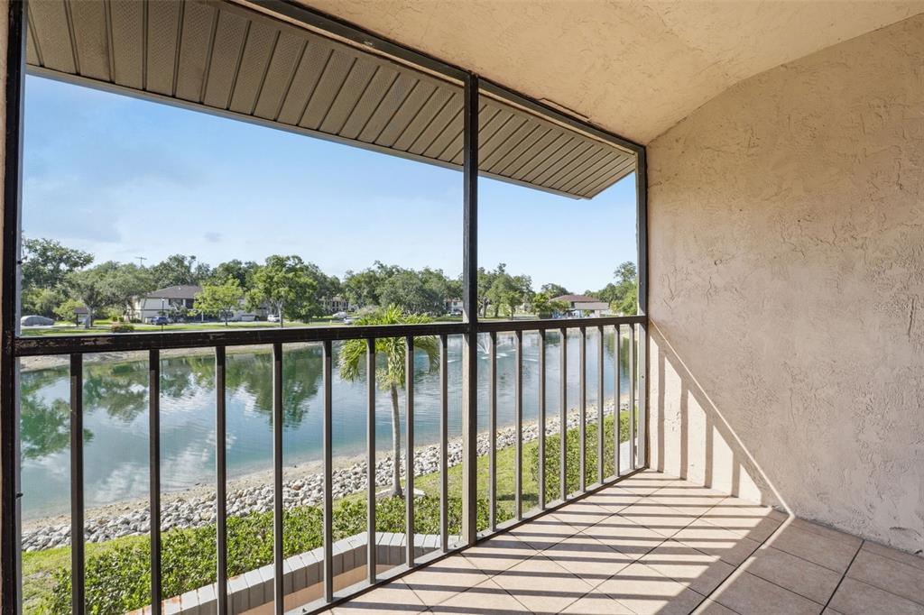 An aerial view shows a multi-story apartment complex situated beside a pond with a fountain — 19505 QUESADA AVENUE UNIT AA204, PORT CHARLOTTE, FL